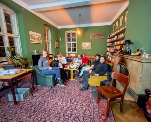 Gruppenfoto des Medienstammtischs im Coconat: mehrere Teilnehmer sitzen gemütlich im Salon zusammen, mit Beamer, Snacks und Bücherecke im Hintergrund.